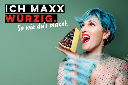 Werbesujet für den Käse «Der scharfe Maxx». Frau mit blau gefärbten Haaren, die Käsestück in der Hand hält.